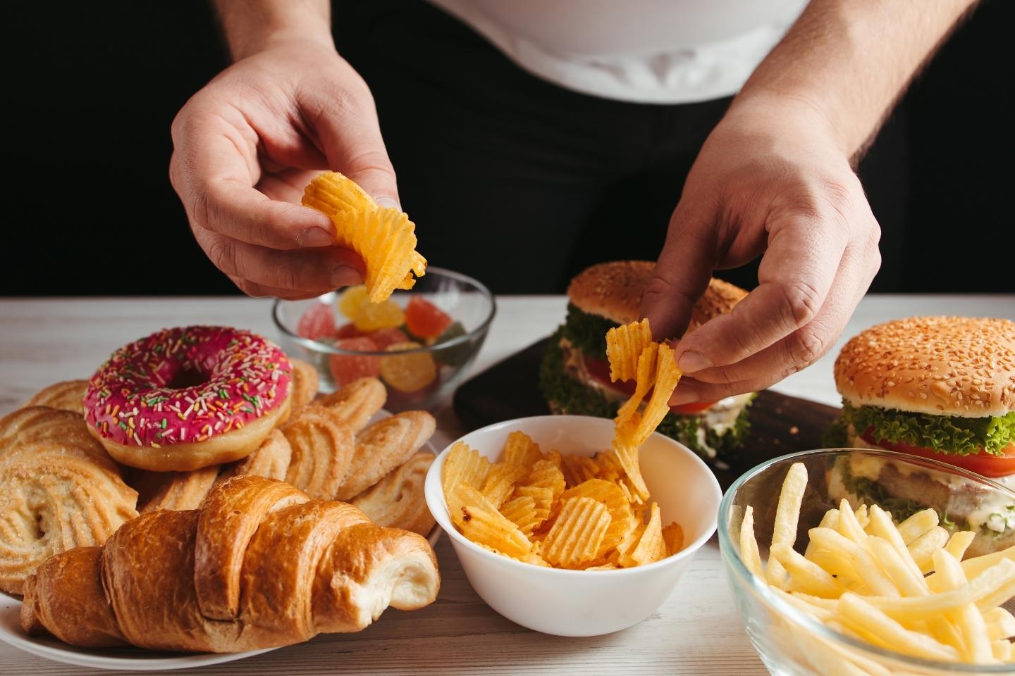Slika čovjek koji se prejeda nezdravom hranom (hamburger, pomfrit, čips, krafne, bomboni, peciva)