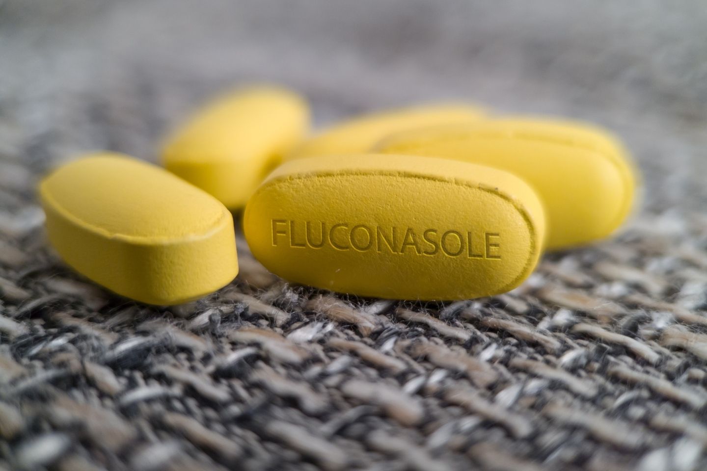 Žuta tableta s natpisom flukonazol na pletenoj podlozi.