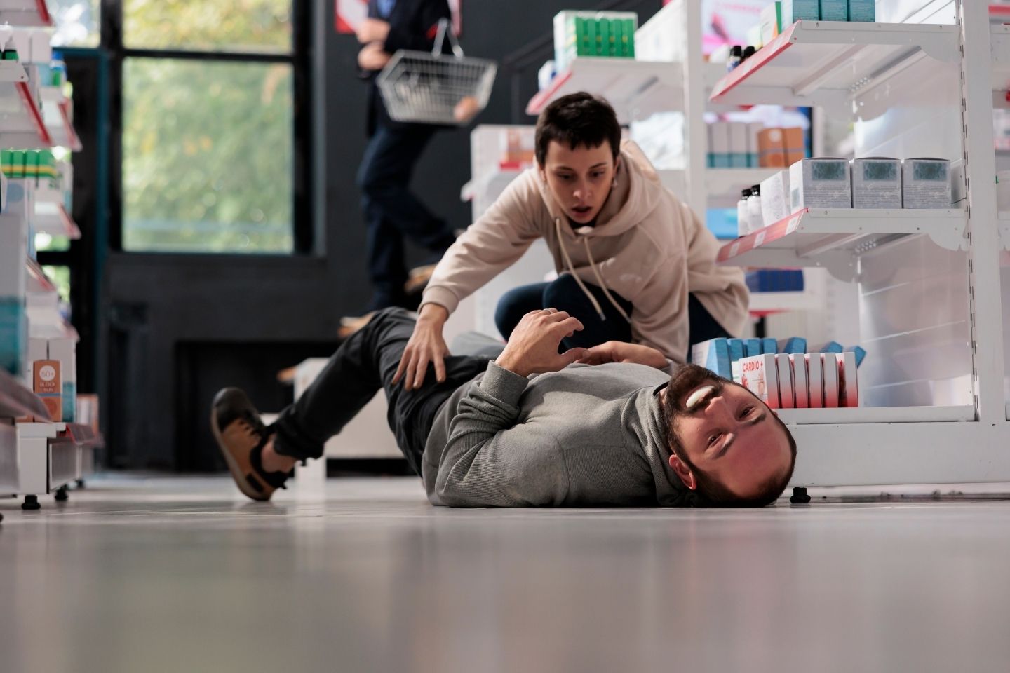 Prestravljena žena pruža prvu pomoć muškarcu na podu ljekarne koji ima epileptični napad