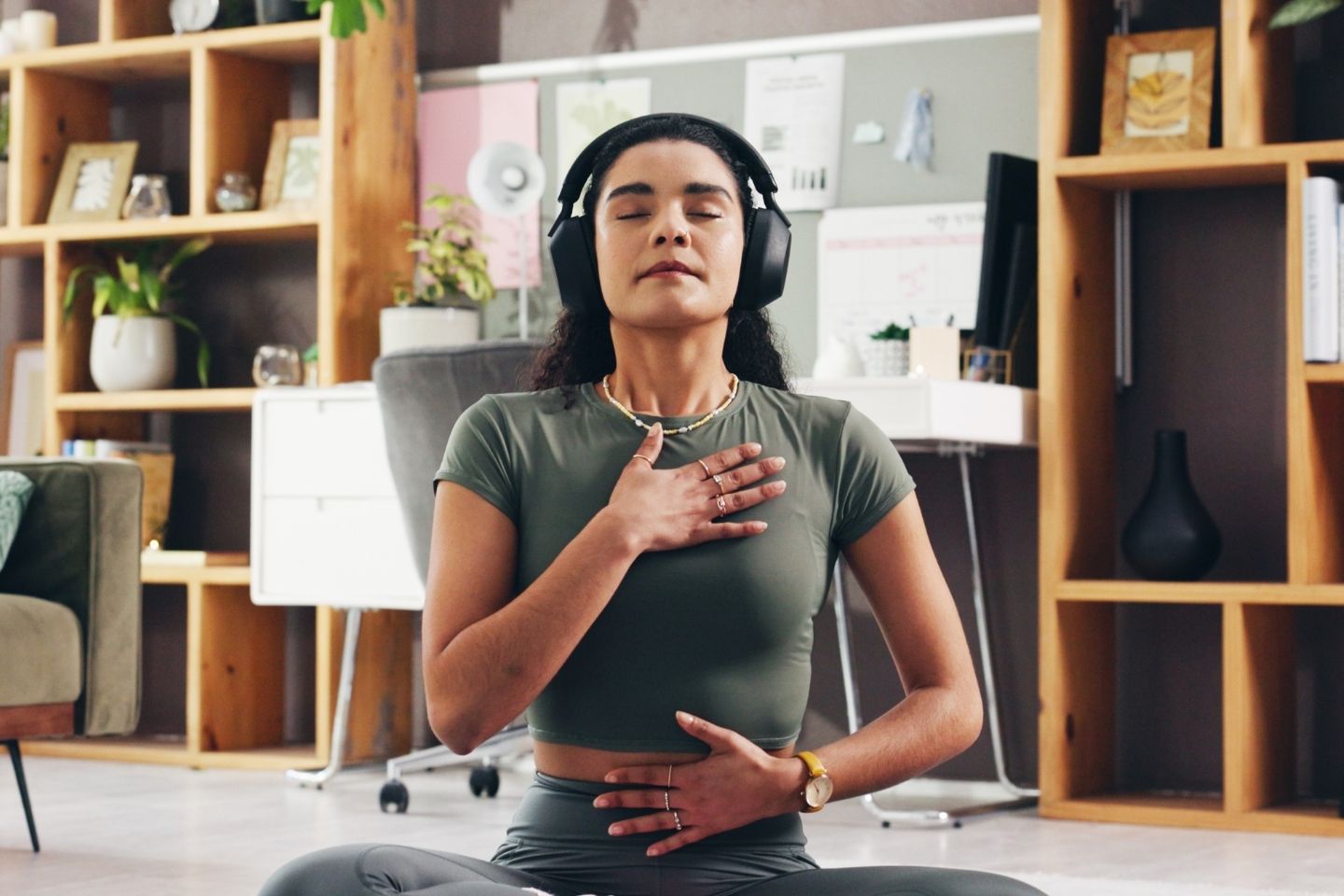 Slika mlade žene sa slušalicama na ušima koja prakticira mindfulness u zatvorenom prostoru.